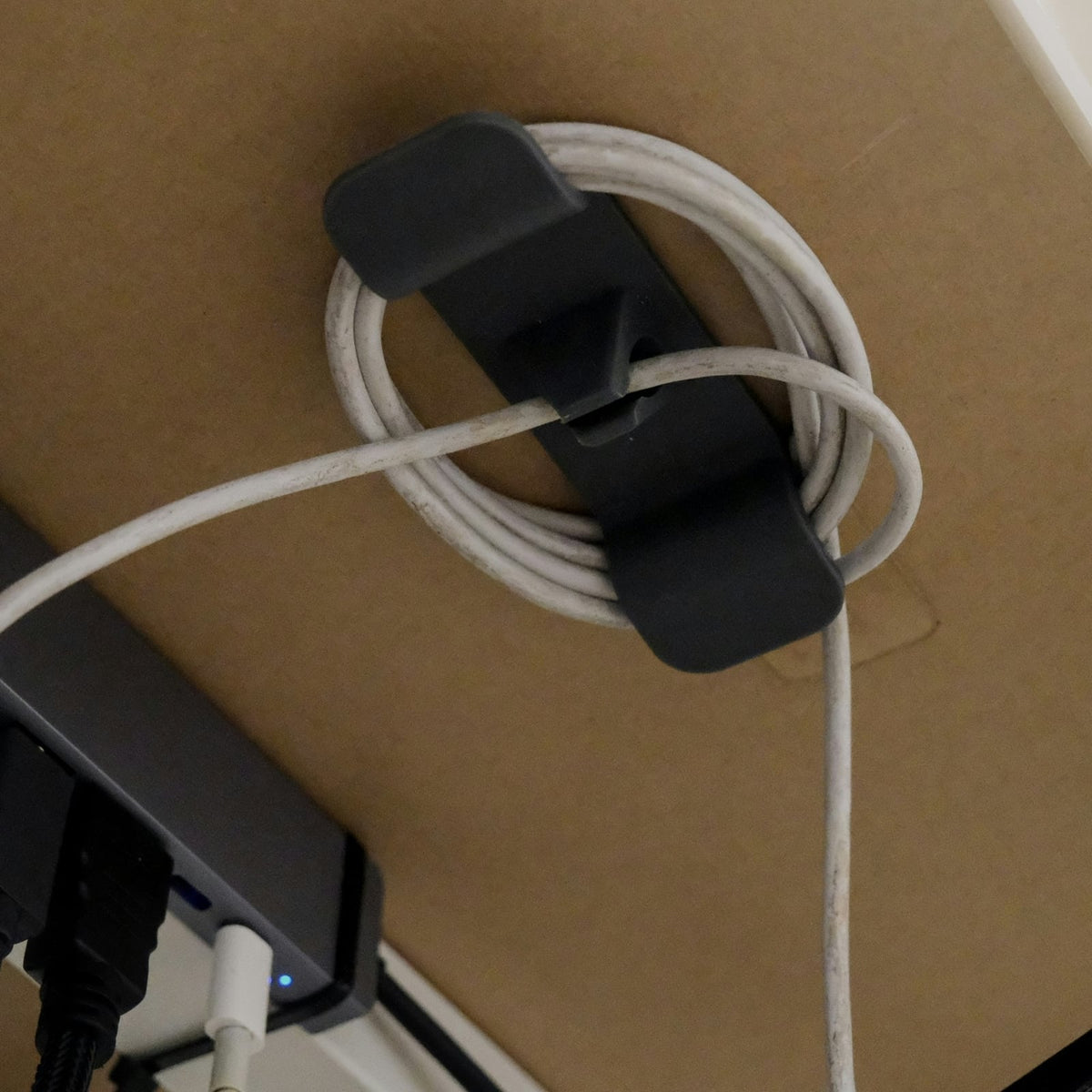 Cable control clip holding coiled cable under a desk